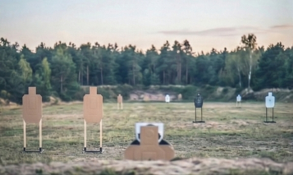 A field with life-size targets set up for marksmanship training, with a forest in the background