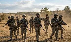 Група військовослужбовців у повному екіпіруванні виконує тактичне пересування відкритим полем у сонячний день під час відпрацювання польової місії